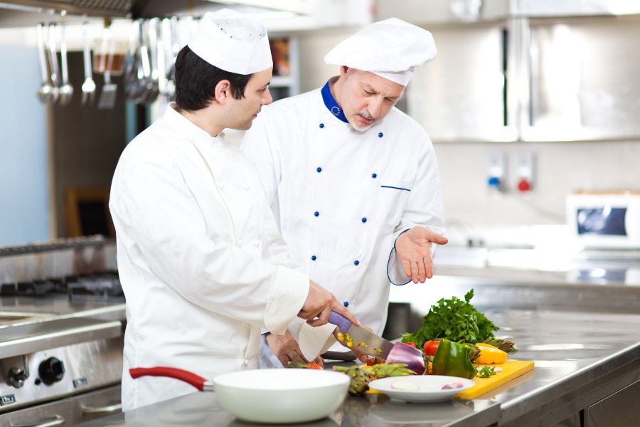 head chef training new employee on food prep in kitchen
