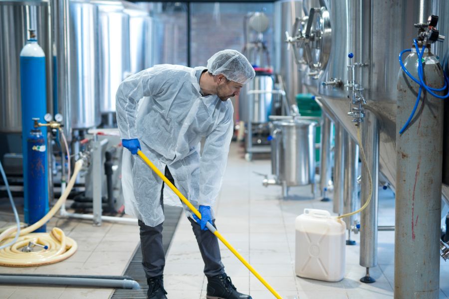 worker in protective uniform cleaning food processing plant