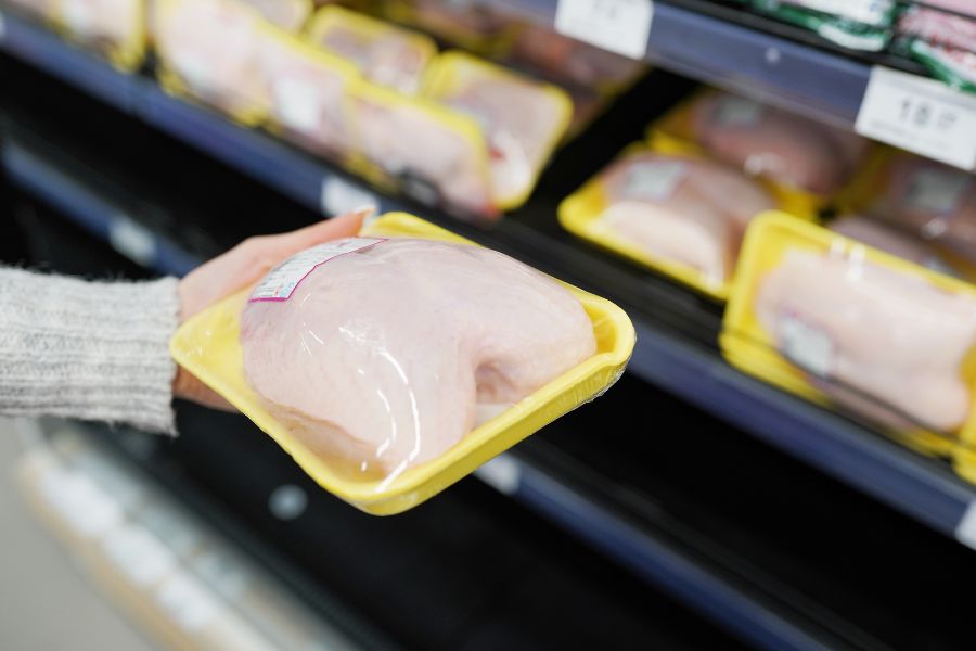 woman choosing packed chicken meat in supermarket
